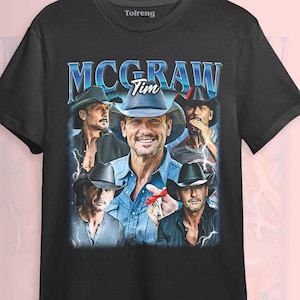 Puede incluir: Camiseta negra con un collage de imágenes de Tim McGraw, el nombre "McGraw" en azul y "Tim" en blanco. El diseño tiene un estilo vintage y retro.