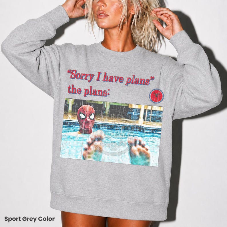 May include: A sport grey crewneck sweatshirt featuring the red text "Sorry I have plans" and "the plans:" above a rectangular graphic of a person wearing a red and blue Spider-Man mask in a swimming pool with feet visible in the foreground.