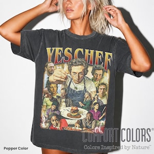 May include: A charcoal grey short-sleeve t-shirt featuring a vintage-style graphic print with the text YES CHEF at the top. The design includes a collage of various characters and a central figure holding a fork over a plated dish of food.