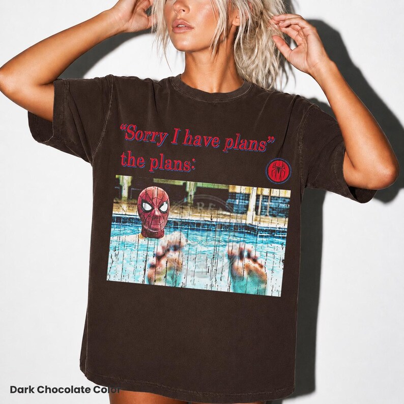 May include: A dark chocolate brown short-sleeve t-shirt featuring the red text "Sorry I have plans" and "the plans:" above a graphic of a person wearing a red spider mask in a swimming pool, with a small red and blue spider logo on the right.