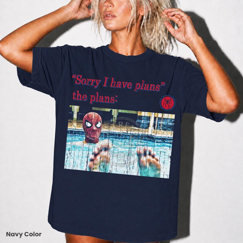 May include: A navy blue short-sleeve t-shirt featuring the red text "Sorry I have plans" and "the plans:" above a graphic of a person wearing a Spider-Man mask in a swimming pool, with a small red and blue circular spider logo on the right side.