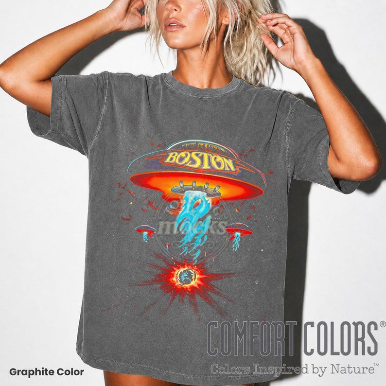 May include: Graphite-colored t-shirt featuring a graphic of a UFO with the word "BOSTON" on it. The design includes a red and orange UFO with blue and white elements, and the Comfort Colors logo is visible.