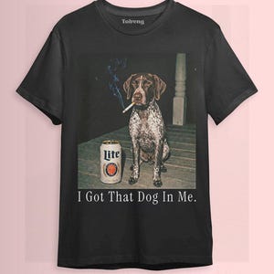 May include: Black t-shirt featuring a dog with a cigarette in its mouth and a beer can. The text "I Got That Dog In Me" is printed below the image. The shirt has a crew neck and short sleeves.