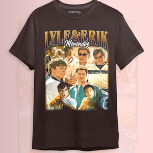 May include: Dark brown t-shirt with a collage of images and the text "LYLE & ERIK Menendez" in gold. The images are of several men in various poses. The shirt has a crew neck and short sleeves.