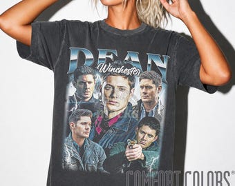 May include: A charcoal gray short-sleeve t-shirt featuring a graphic print of the character Dean Winchester from the television show Supernatural. The design includes multiple portraits of the character, lightning bolts, and the text DEAN.