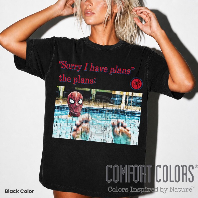 May include: A black short-sleeve t-shirt featuring the red text "Sorry I have plans" and "the plans:" above a graphic of Spider-Man in a swimming pool. A small red and blue circular spider logo is positioned to the right of the text.