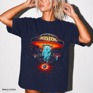 May include: Navy blue t-shirt featuring a graphic of a UFO with the word "BOSTON" on it, set against a starry space background. The design includes a red and orange UFO with blue and white energy beams. The text "Navy Color" is at the bottom left.