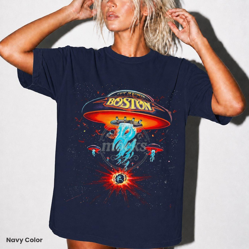 May include: Navy blue t-shirt featuring a graphic of a UFO with the word "BOSTON" on it, set against a starry space background. The design includes a red and orange UFO with blue and white energy beams. The text "Navy Color" is at the bottom left.