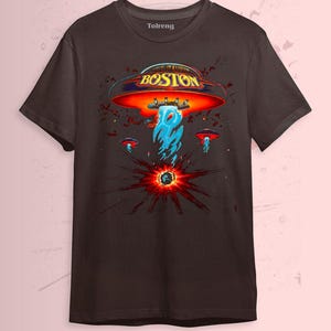 May include: Dark brown t-shirt featuring a graphic design with the word "BOSTON" in gold lettering on a red and orange UFO. The design includes blue flames and smaller UFOs, with a burst of red and black radiating from a central point.