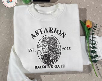 Könnte beinhalten: Weißes Sweatshirt mit einer schwarz-weißen Porträtillustration einer Person, dem Namen "Astarion" und dem Text "Baldur's Gate". Der Text "EST. + 2023" ist ebenfalls vorhanden. Das Sweatshirt hat einen Rundhalsausschnitt und lange Ärmel.
