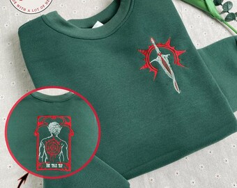 May include: A dark green sweatshirt with red embroidered designs. The front design features a sword and sun. The back design features a figure with the text "The Tall Elf".