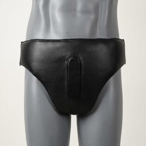 May include: A black faux leather athletic supporter or groin guard featuring a smooth, matte finish and a reinforced, padded central vertical panel. The protective gear has a wide waistband and a contoured shape designed for coverage and support.