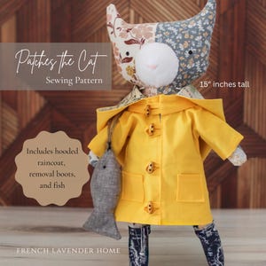 May include: A 15-inch tall fabric cat doll named Patches the Cat, featuring a floral patterned head and wearing a bright yellow hooded raincoat with toggle buttons and pockets. The doll includes removable boots and a small grey fish accessory. The text reads Patches the Cat Sewing Pattern, Includes hooded raincoat, removal boots, and fish, and FRENCH LAVENDER HOME.