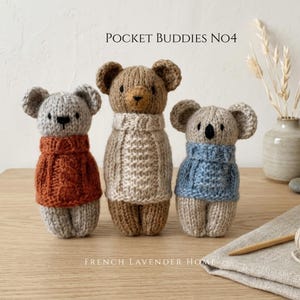May include: Three small hand-knitted animal figures labelled POCKET BUDDIES NO4 and FRENCH LAVENDER HOME. The left figure is a grey bear in a rust jumper, the centre is a brown bear in a cream jumper, and the right is a grey koala in a blue jumper.