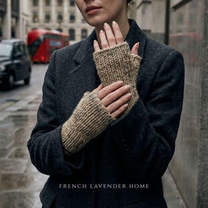Könnte beinhalten: Ein Paar beigefarbene, grob gestrickte fingerlose Handschuhe mit gerippter Textur. Die Handschuhe werden über einem dunkel anthrazitfarbenen Wollblazer getragen. Der Text "FRENCH LAVENDER HOME" ist unten mittig in Weiß aufgedruckt.