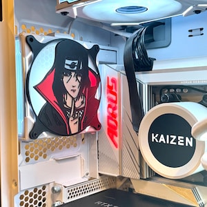 Peut inclure: Un boîtier d'ordinateur blanc avec un ventilateur noir et rouge représentant un personnage d'anime. Le ventilateur est marqué "AORUS". Le boîtier possède également un ventilateur blanc et noir marqué "KAIZEN".