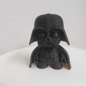Puede incluir: Una figura negra de Darth Vader de Star Wars, impresa en 3D. La figura es pequeña y tiene un diseño detallado.