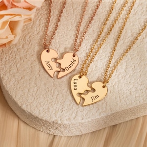 May include: Two matching heart-shaped pendant necklaces, one in rose gold and the other in gold. Each pendant is split into two pieces, with names engraved on each half. The rose gold necklace has "Amy" and "David" engraved. The gold necklace has "Luna" and "Jim" engraved.