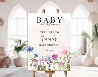 May include: A white sign with a floral design and the text "BABY in bloom" and "WELCOME TO Teresa's BABY SHOWER APRIL 20, 2023".