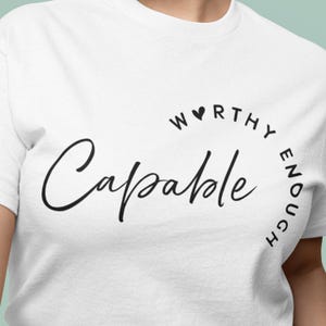 May include: White t-shirt with the words "Capable" in a cursive font and "Worthy Enough" in a semi-circle above and to the right. The shirt is made of a soft material.
