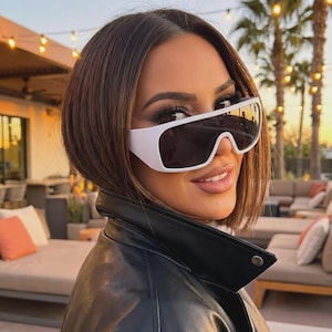 May include: Oversized shield sunglasses featuring a thick white plastic frame and dark, reflective lenses. The design has a continuous, wraparound lens shape that covers the upper portion of the face, providing a bold, modern look with clean lines.