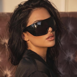 May include: Oversized shield sunglasses featuring a single continuous black lens and a thick black frame. The design covers the upper portion of the face with a wrap-around style, providing a bold, solid black appearance across the eyes and bridge.