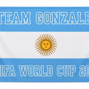 May include: A rectangular flag featuring the horizontal light blue and white stripes of the Argentine flag with a central yellow sun emblem. The text TEAM GONZALEZ is printed in white block letters at the top and FIFA WORLD CUP 2026 at the bottom.