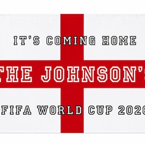 May include: A rectangular white fabric banner featuring a red cross, with white ties at the top corners. The text reads IT'S COMING HOME, THE JOHNSON'S, and FIFA WORLD CUP 2026 in black and red block lettering across the centre of the flag design.
