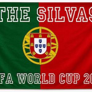 May include: A rectangular flag featuring a vertical split of dark green and red. Centered is the Portuguese coat of arms. The white text THE SILVAS appears at the top, and FIFA WORLD CUP 2026 is printed in white at the bottom in a block font.