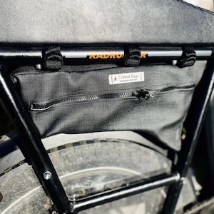 Pode incluir: Bolsa preta para bagageiro de bicicleta com zíper e uma pequena etiqueta que diz "Conrad Bags Handmade in the USA".
