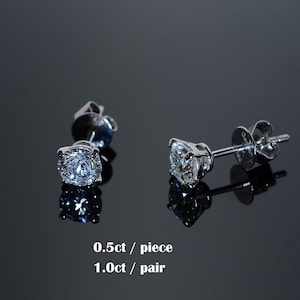 May include: A pair of diamond stud earrings with a brilliant cut. The earrings are set in a silver metal and reflect light. The text on the image reads "0.5ct / piece 1.0ct / pair".