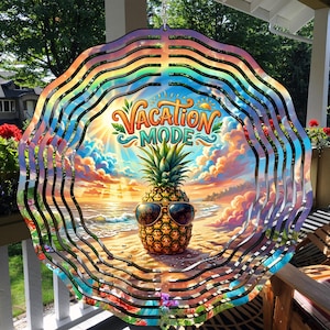 May include: A colorful, layered metal wind spinner with a beach scene featuring a pineapple wearing sunglasses. The text "Vacation Mode" is displayed in a whimsical font. The spinner has a rainbow-colored wavy border.