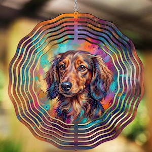 Könnte beinhalten: Ein dekorativer, runder Windspinner mit einem Aquarellporträt eines Dackelhundes. Der Hund hat braunes und schwarzes Fell mit einem farbenfrohen Hintergrund aus Blau-, Rosa- und Orangetönen. Der äußere Rahmen hat ein geschichtetes, wellenförmiges Design.