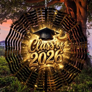 May include: A decorative, circular wind spinner with the text "Class of 2026" in gold lettering. The design includes a graduation cap and a burst of golden light. The spinner is black and gold and is hanging outdoors.