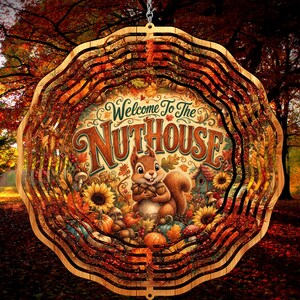 Puede incluir: Un molinillo de viento circular con patrón de veta de madera y una ilustración central de una ardilla sosteniendo bellotas. El texto Welcome To The NUTHOUSE está impreso en una fuente decorativa. El diseño incluye girasoles, calabazas y hojas de otoño.