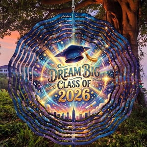 May include: A round, layered wind spinner with a graduation theme. The design features a graduation cap, the words "Dream Big Class of 2026", and a cityscape silhouette, all in vibrant colors against a starry background.