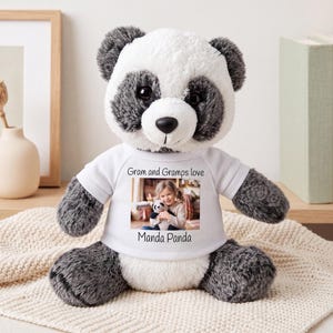 May include: A plush panda bear with black and white fur wearing a white t-shirt. The shirt features a printed photograph of a young child holding a small panda toy, with the text "Gram and Gramps love" above the photo and "Manda Panda" below.