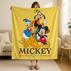 May include: Yellow blanket featuring Mickey Mouse, Donald Duck, Goofy, and Pluto. The blanket has the words "MICKEY and friends" in black with red and green accents. The blanket is held up by a person.