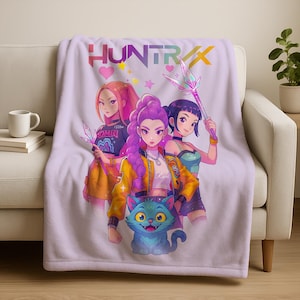 May include: A light purple throw blanket featuring a colorful anime-style illustration of three women and a blue cat. The blanket has the word "HUNTRAX" in rainbow colors across the top.