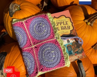 May include: A rectangular crochet book cover featuring four squares with purple circular smiley face motifs on a bright pink background, bordered by a light green scalloped edge, partially covering a book titled Apple B&B.