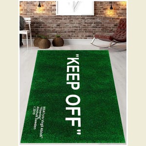 Puede incluir: Una alfombra verde con el texto "KEEP OFF" en letras blancas. El texto est&aacute; en negrita, sin serifas. La alfombra est&aacute; hecha de un material suave y mullido y tiene una textura realista similar a la hierba.