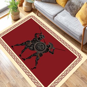 May include: A rectangular area rug featuring a burgundy field with a black and tan illustration of two warriors in combat. The rug has a cream-colored border with a repeating geometric pattern. The design is reminiscent of ancient Greek art.