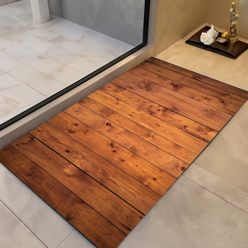 K&ouml;nnte beinhalten: Eine rechteckige Fu&szlig;matte mit Holzplanken-Design. Die Matte zeigt ein Muster aus parallelen, dunkelbraunen Holzplanken mit sichtbaren Knoten und Maserungen. Die Matte liegt auf einem hell gefliesten Boden in der N&auml;he einer Glast&uuml;r.