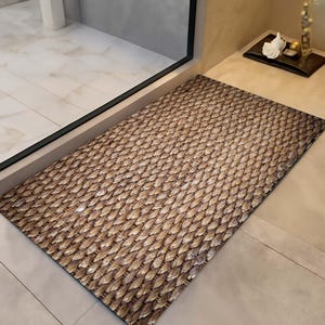 May include: A rectangular doormat with a woven, textured pattern in shades of brown and tan. The mat is placed in front of a glass door, suggesting an entryway or bathroom setting. The design resembles natural fibers.