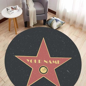May include: A round black and red rug with a large red star in the center. The star has a gold outline and the words "YOUR NAME" written on it. The rug has a speckled texture.