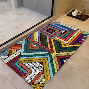 May include: Rectangular doormat with a vibrant, geometric design. The mat features a repeating pattern of colourful, stitched lines in shades of red, blue, green, yellow, and purple. The design creates a textured, eye-catching appearance, suitable for an entryway.