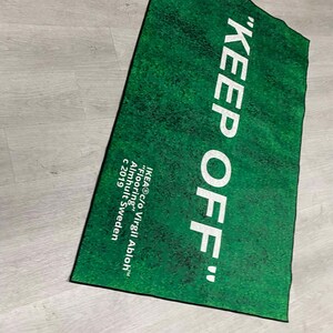 Puede incluir: Una alfombra verde con el texto "KEEP OFF" en letras blancas. La alfombra tambi&eacute;n incluye el texto "IKEA c/o Virgil Abloh&trade;" "Flooring" "Almhult Sweden" "c 2019".