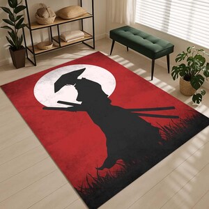 May include: A rectangular rug with a samurai warrior silhouette set against a red background and a large white circle, like a moon. The warrior holds two swords, with grass in the foreground.