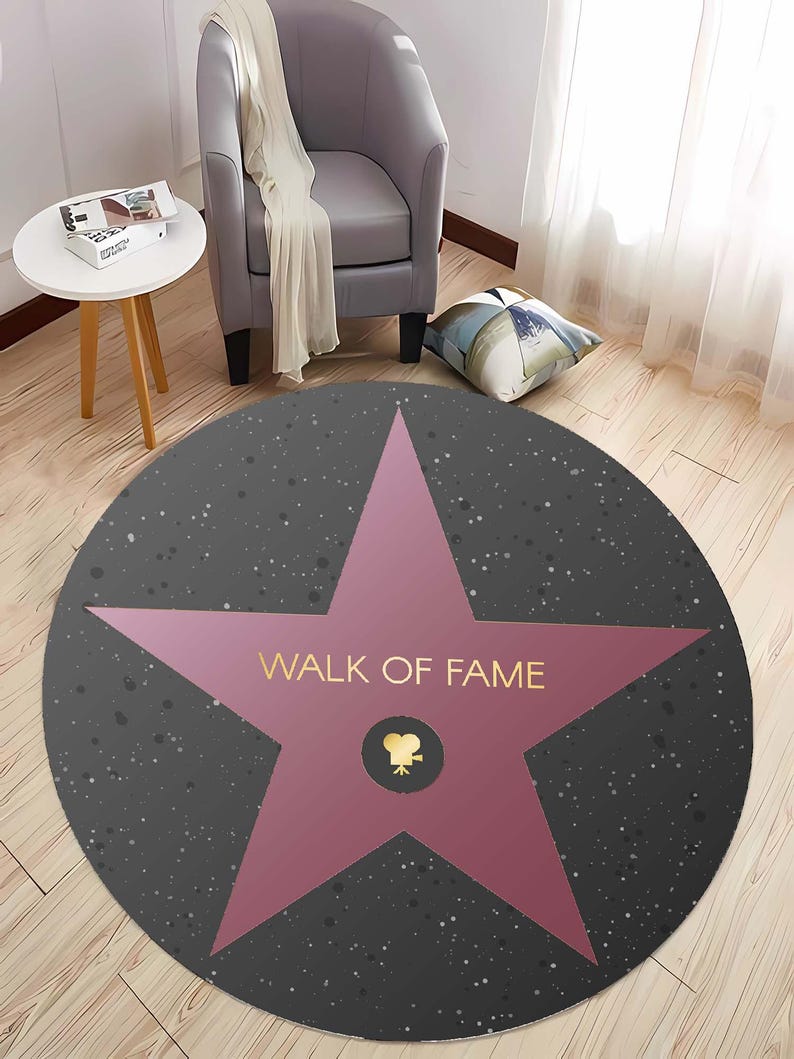 May include: A round, gray and pink rug with a large pink star in the center. The star has the words "Walk of Fame" written on it in gold lettering. The star also has a small gold film camera icon in the center.