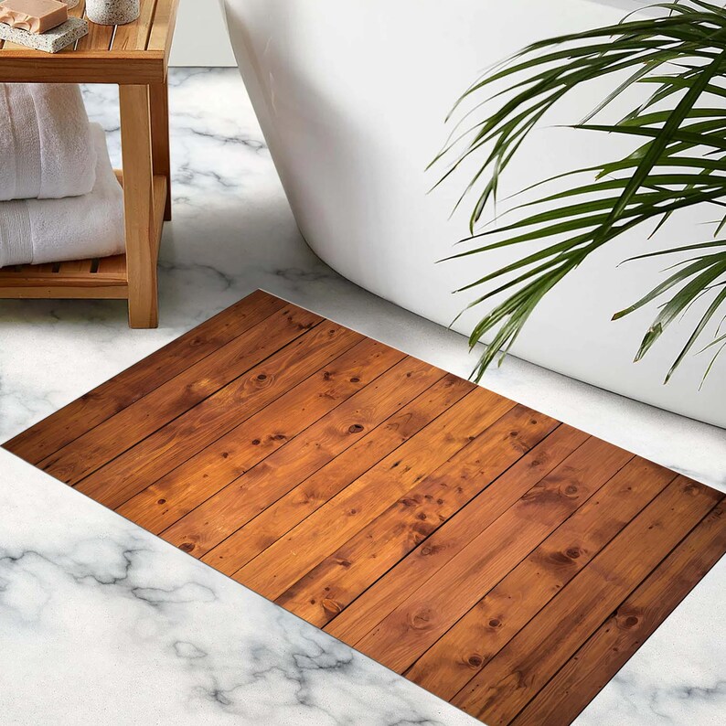 K&ouml;nnte beinhalten: Eine rechteckige Badematte mit Holzplanken-Design. Die Matte ist braun mit verschiedenen Farbt&ouml;nen und Holzmaserungsdetails. Sie liegt auf einem marmorierten Boden in der N&auml;he einer wei&szlig;en Badewanne und eines Holzregals mit Handt&uuml;chern.